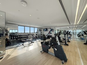 Un gimnasio moderno con equipo de ejercicio, ventanas amplias y una pared de espejos.