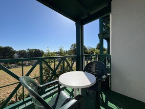 A balcony with a table and chairs, overlooking a grassy area and a mountain. - Le Petit Patio - Downtown (CAMBO LES BAINS)