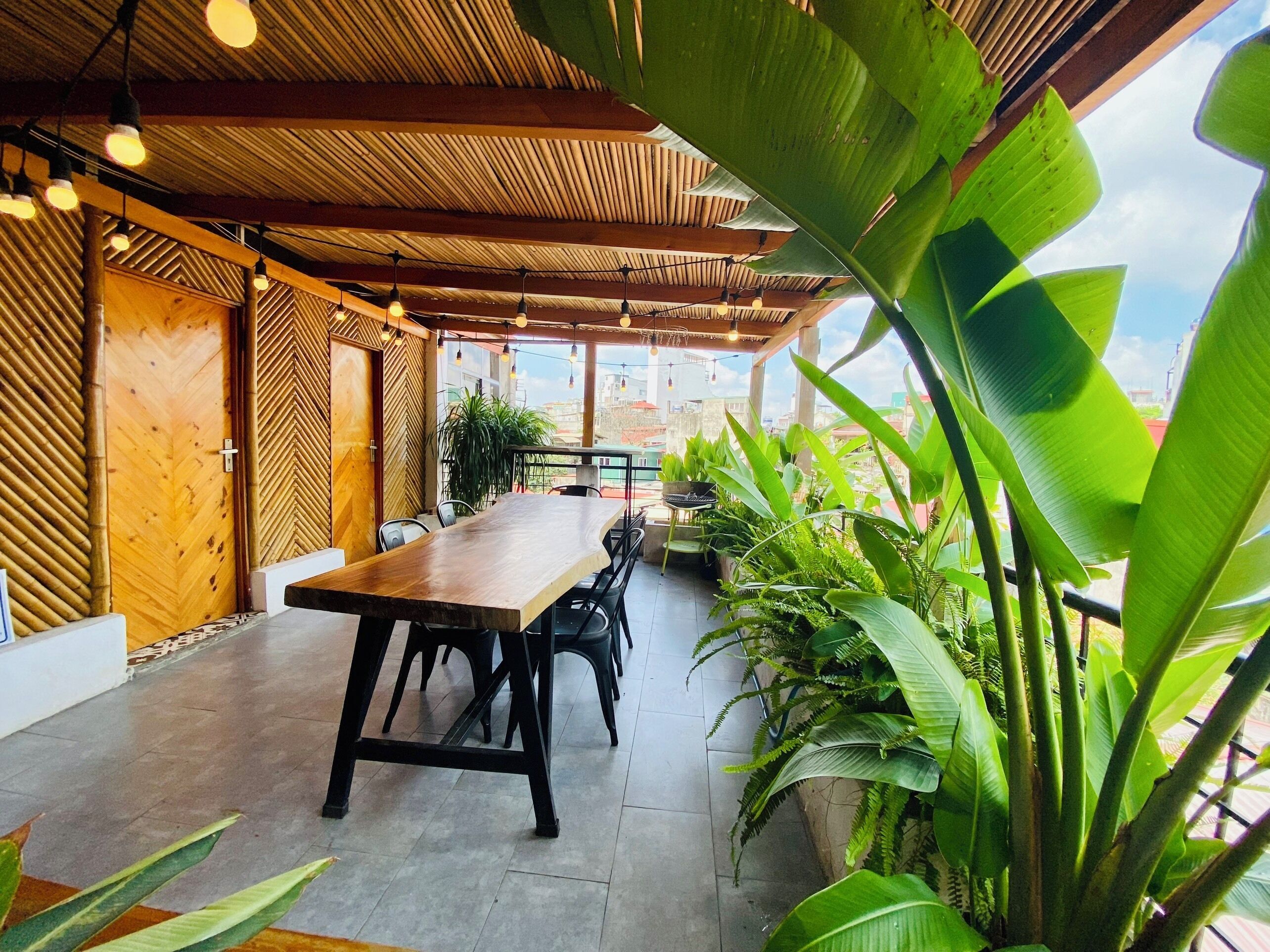 An indoor dining area with a long wooden table, chairs, and potted plants.