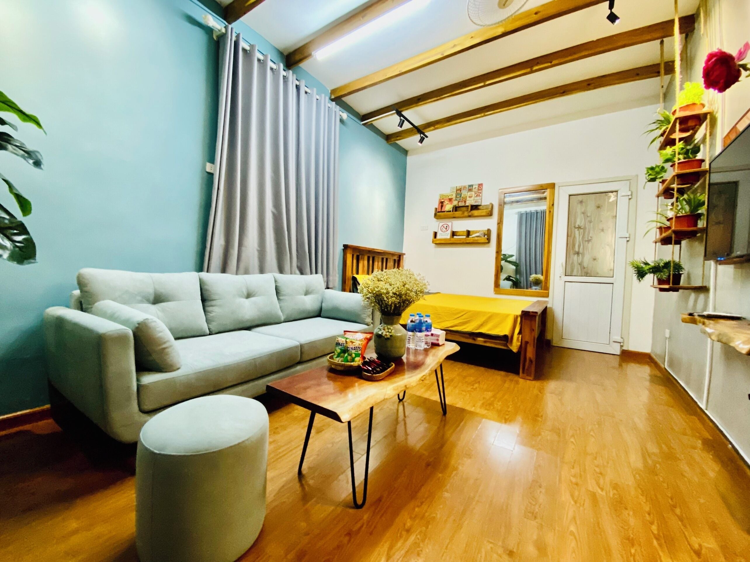 Una sala de estar con sofá, una mesa de centro, un pequeño reposapiés, una cama con edredón amarillo y techo de madera.