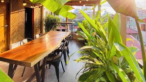 An outdoor dining area with a wooden table and chairs, surrounded by large green plants and a bamboo ceiling. - 3BR Old Quarter Stay | Walk to Lake & Beer Street | Rooftop & Soaking Tub (Hà Nội)