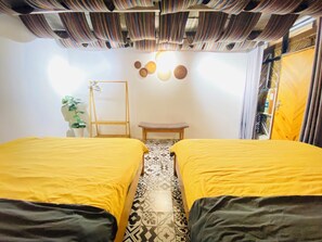 Ein Zimmer mit zwei Betten, einem kleinen Tisch, einer Zimmerpflanze und einer Wand mit runden Verzierungen.