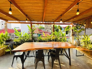 An outdoor dining area with a wooden table and chairs, surrounded by potted plants and a view of buildings. - 3BR Old Quarter Stay | Walk to Lake & Beer Street | Rooftop & Soaking Tub (Hà Nội)