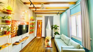 A living room with a wooden ceiling, a flat-screen TV, a sofa, a coffee table, and various potted plants. - 3BR Old Quarter Stay | Walk to Lake & Beer Street | Rooftop & Soaking Tub (Hà Nội)