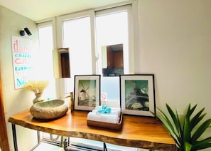 A room with a wooden table displaying framed pictures, a stone bowl with dried flowers, and a wall with a decorative sign. - 3BR Old Quarter Stay | Walk to Lake & Beer Street | Rooftop & Soaking Tub (Hà N ội)