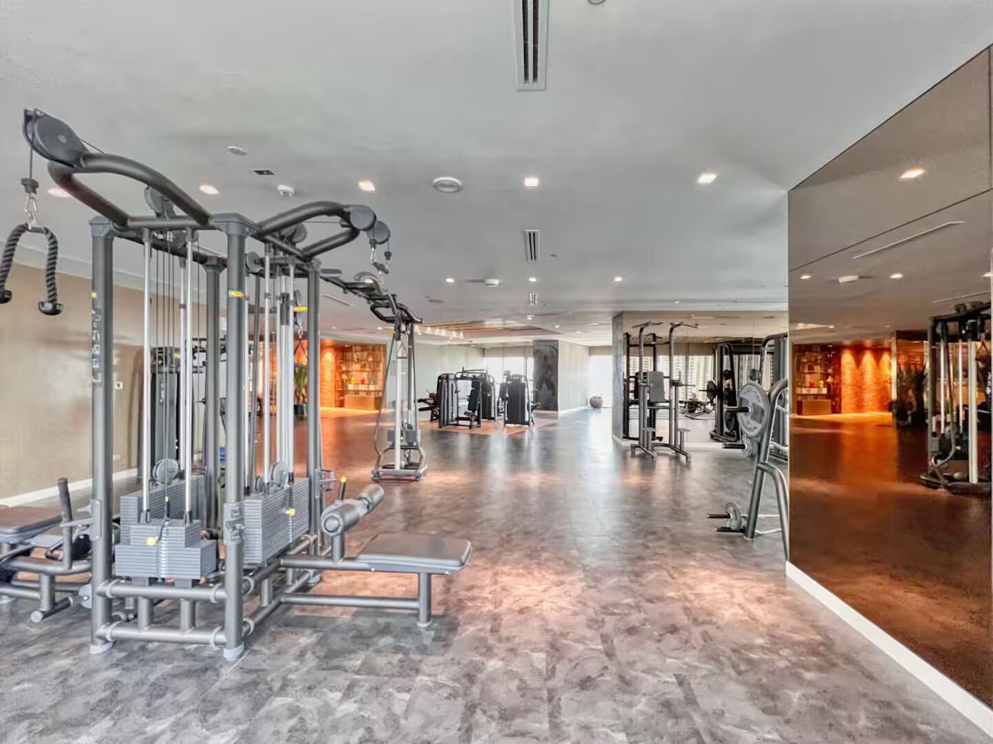 A spacious gym with various exercise machines, a mirrored wall, and a polished floor.