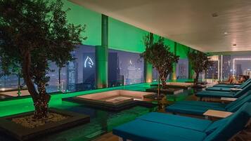Un salón en la azotea con sillones azules, una piscina pequeña y árboles.