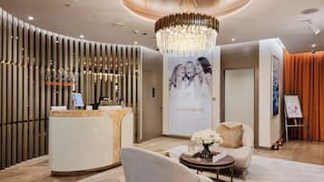 A modern reception area with a reception desk, a chandelier, a seating area with a sofa and armchair, and a wall with a poster.