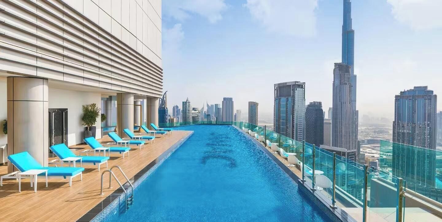 A rooftop infinity pool with lounge chairs and a city skyline view.