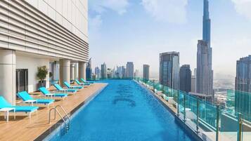 A rooftop infinity pool with lounge chairs and a city skyline view.