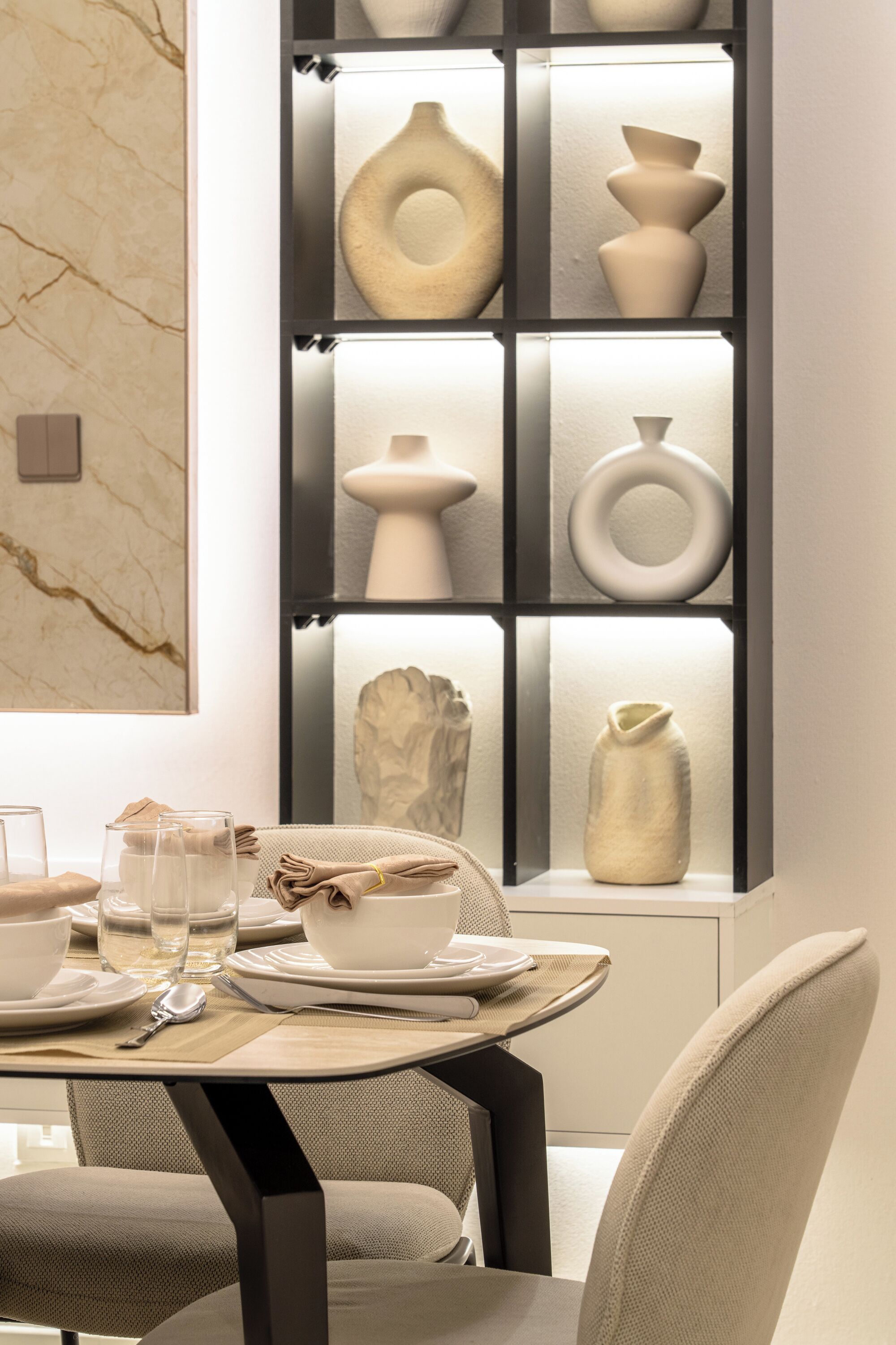 Een moderne eetruimte met een tafel gedekt voor twee personen, een marmeren wand en een verzameling vazen.