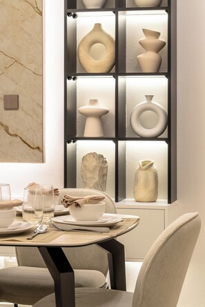 A modern dining area with a table set for two, a marble wall, and a display of vases. - Gogoto11 2BR Premium Infinity Pool & Burj View (Dubai)
