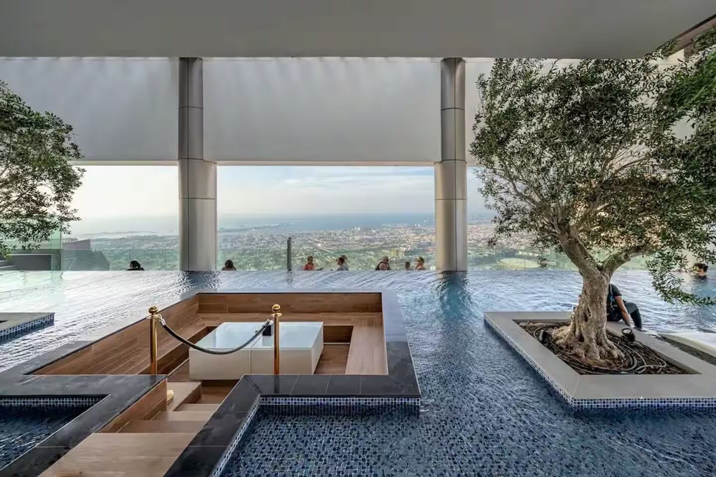 Une piscine à débordement située sur le toit, offrant une vue sur la ville, et entourée d’arbres et d’une architecture moderne.