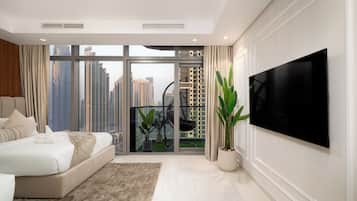 A modern bedroom with a large bed, a TV, and a balcony with a view of high-rise buildings.