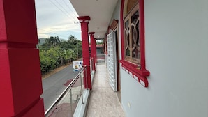 Un pasillo con pilares rojos, piso de baldosas y vista a la calle.