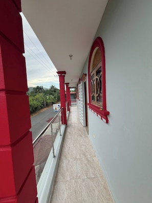 A corridor with red pillars, a tiled floor, and a view of the street outside.