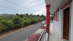 Un balcón con vistas a una carretera y vegetación, un letrero de café, y una puerta a la derecha.
