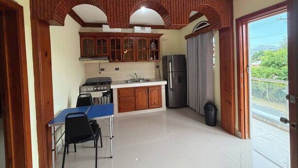 Una cocina con armarios de madera, estufa a gas, refrigerador y mesa de comedor con sillas.