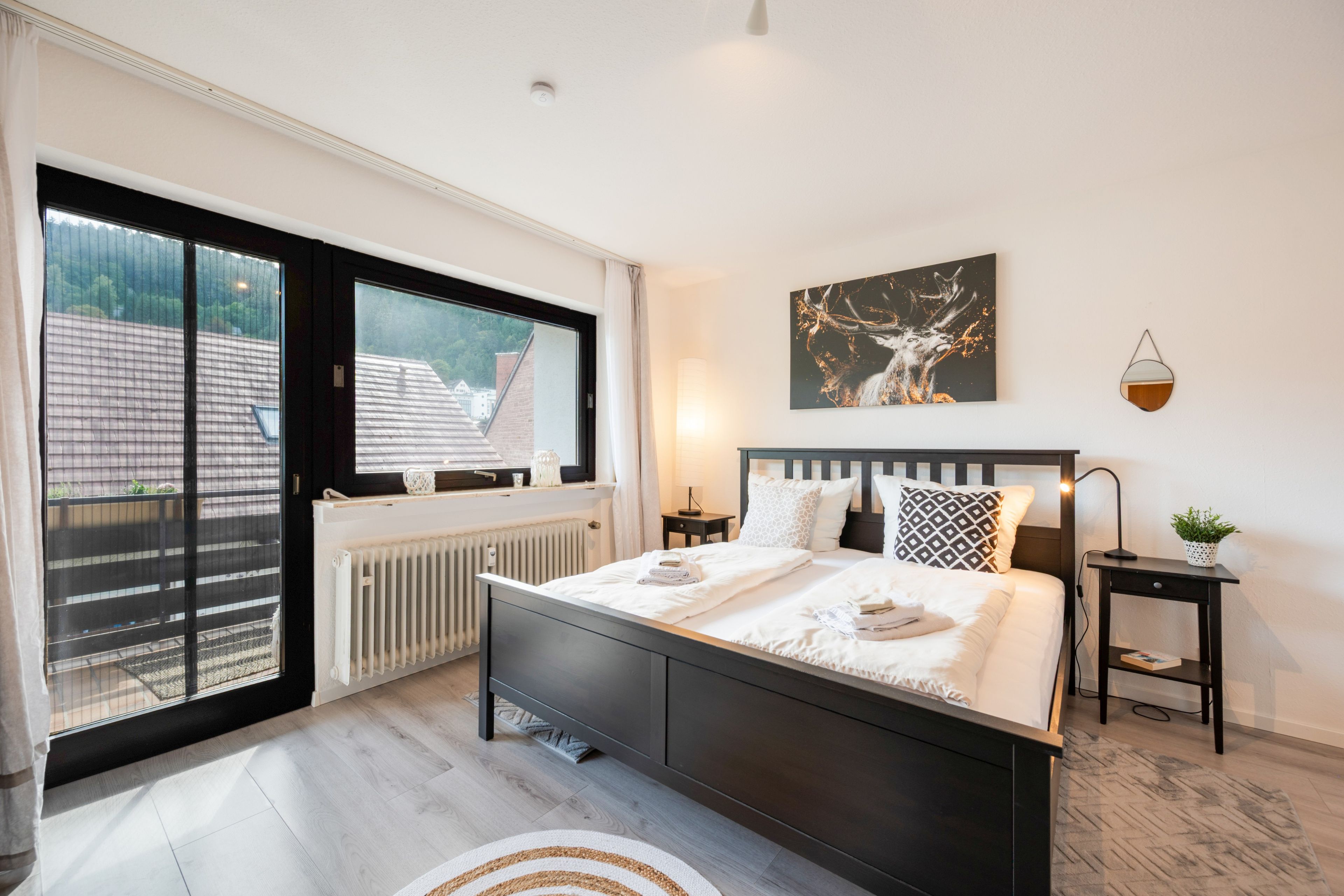 Ein Schlafzimmer mit einem großen Bett, einem Fenster mit Blick auf Gebäude, einem Heizkörper und einem an der Wand hängenden Kunstwerk.