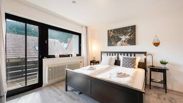 Ein Schlafzimmer mit einem großen Bett, einem Fenster mit Blick auf Gebäude, einem Heizkörper und einem an der Wand hängenden Kunstwerk.