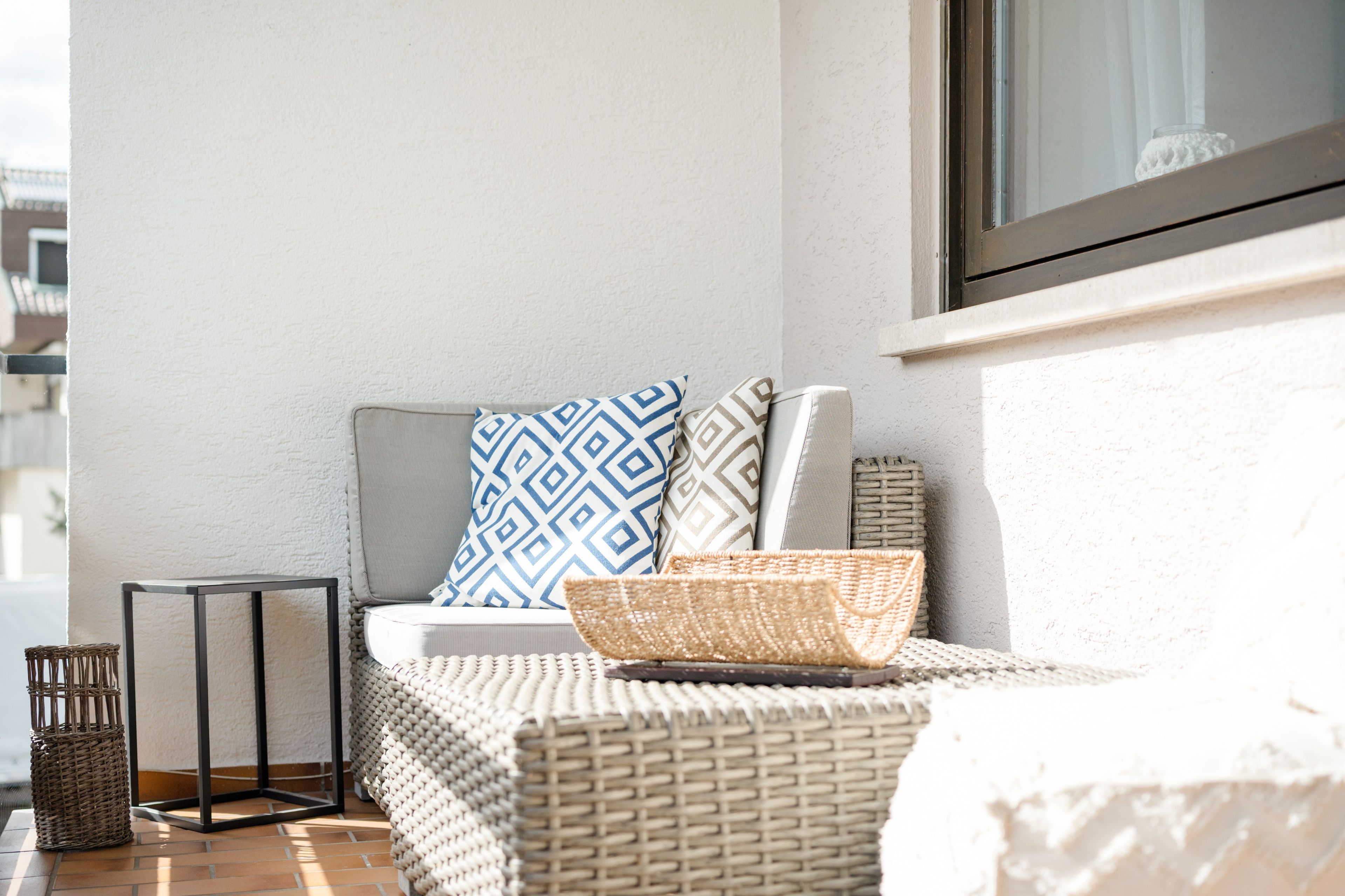 A balcony with a wicker sofa, a small table, and a basket.
