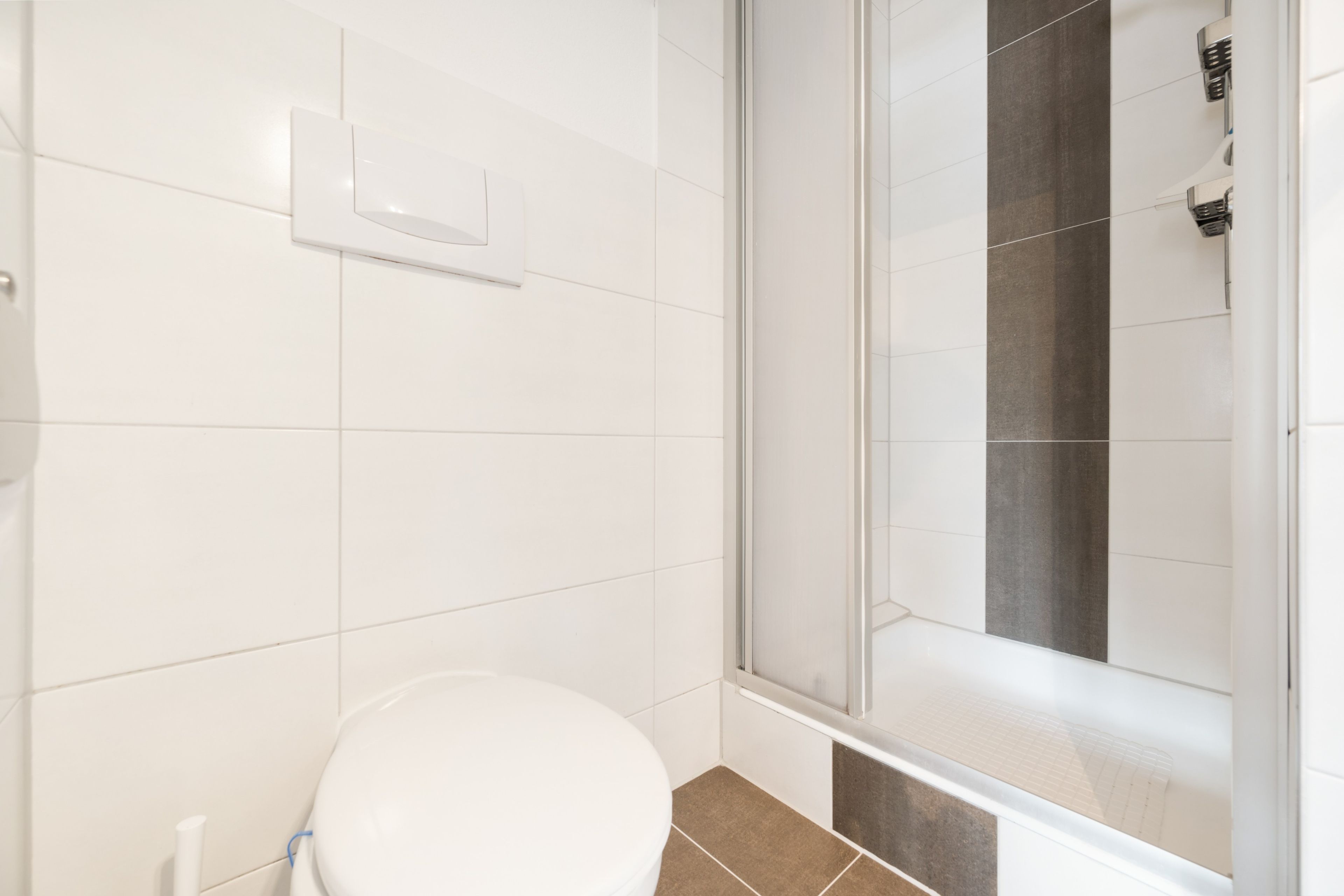 A bathroom with a toilet, a shower enclosure, and a white tiled wall.