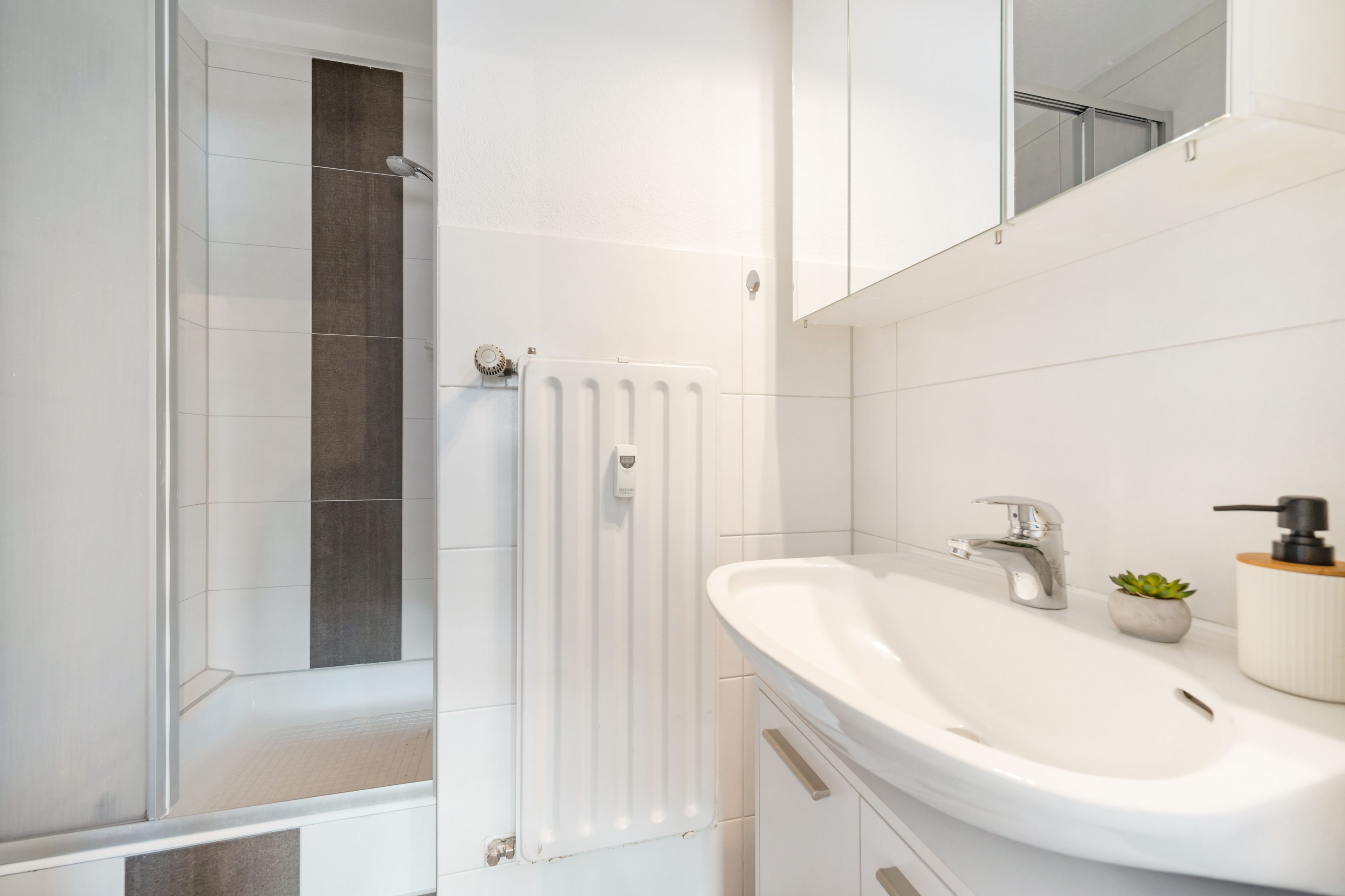 Ein modernes Badezimmer mit Dusche, einem weißen Waschbecken und einem Spiegel.