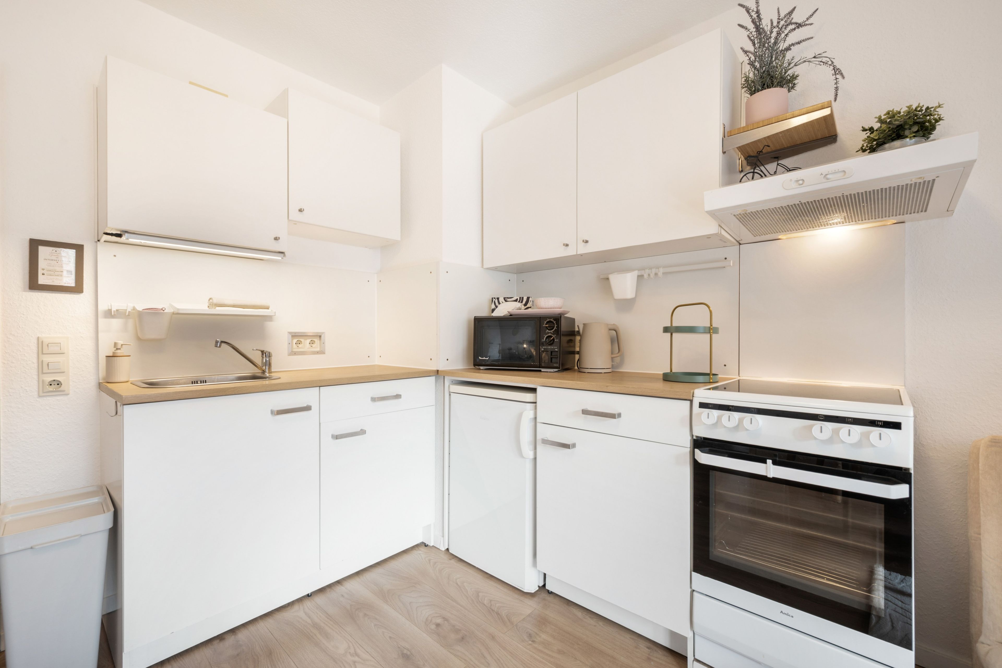 Een kleine keuken met witte kastjes, een magnetron, een koffiezetapparaat en een fornuis.