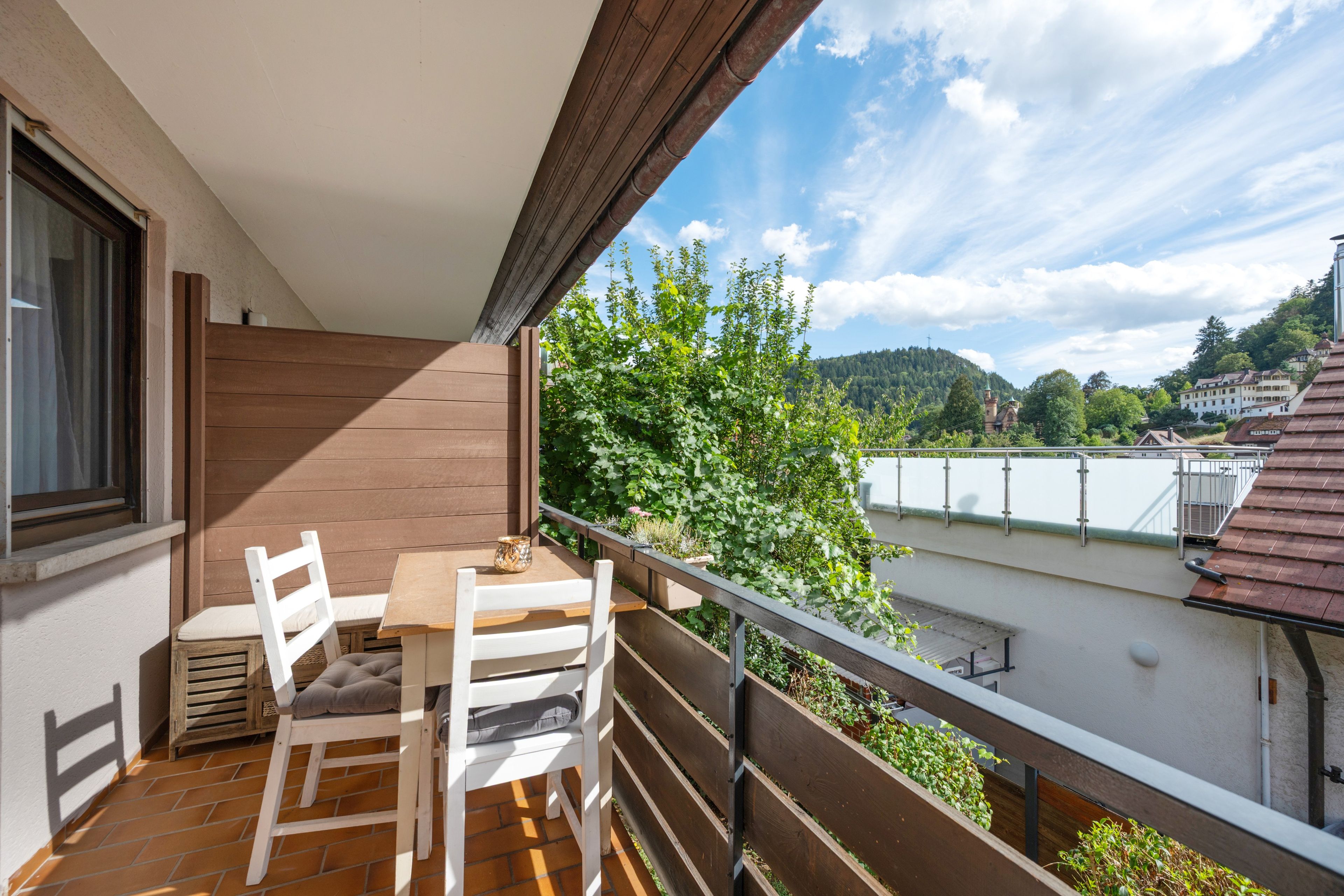 Een balkon met een tafel en stoelen, met uitzicht op een woonwijk met huizen en groen.