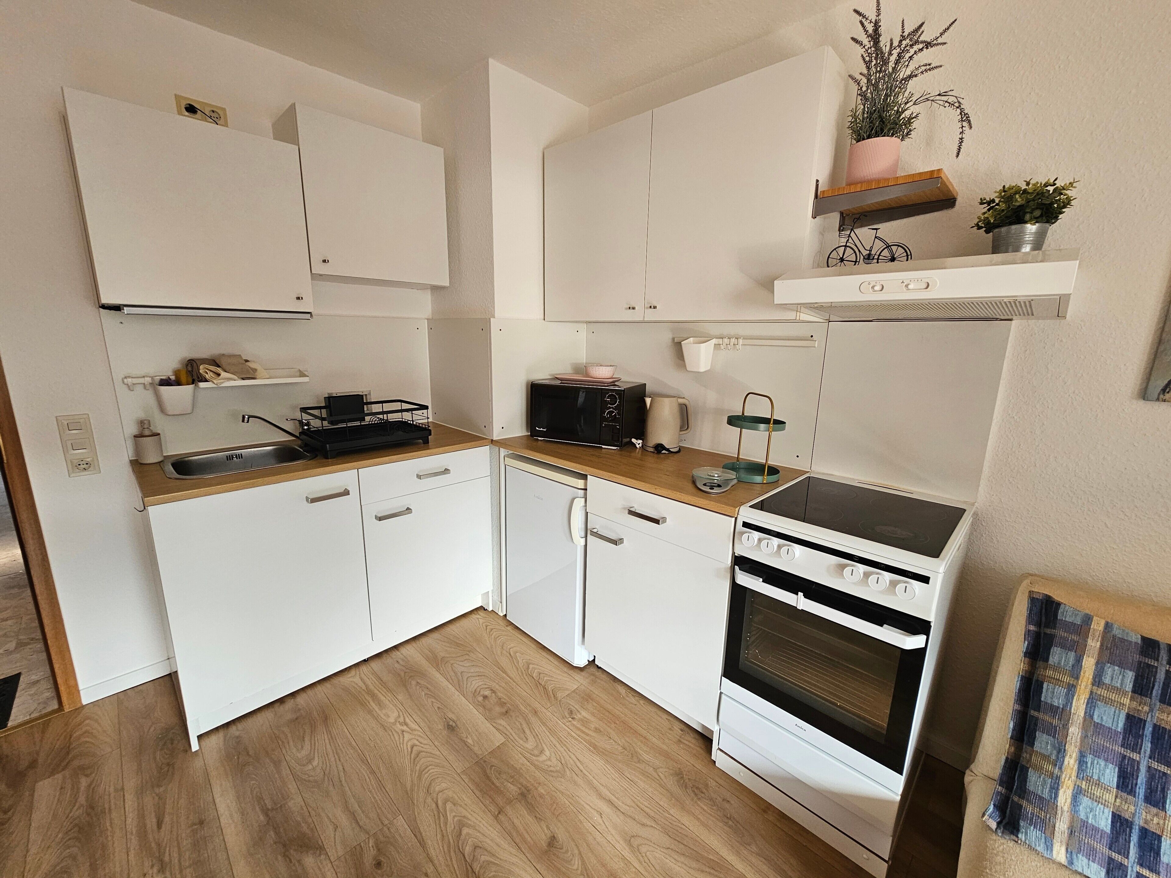 Una cocina compacta con armarios blancos, encimera de madera, horno empotrado y un lavamanos pequeño.