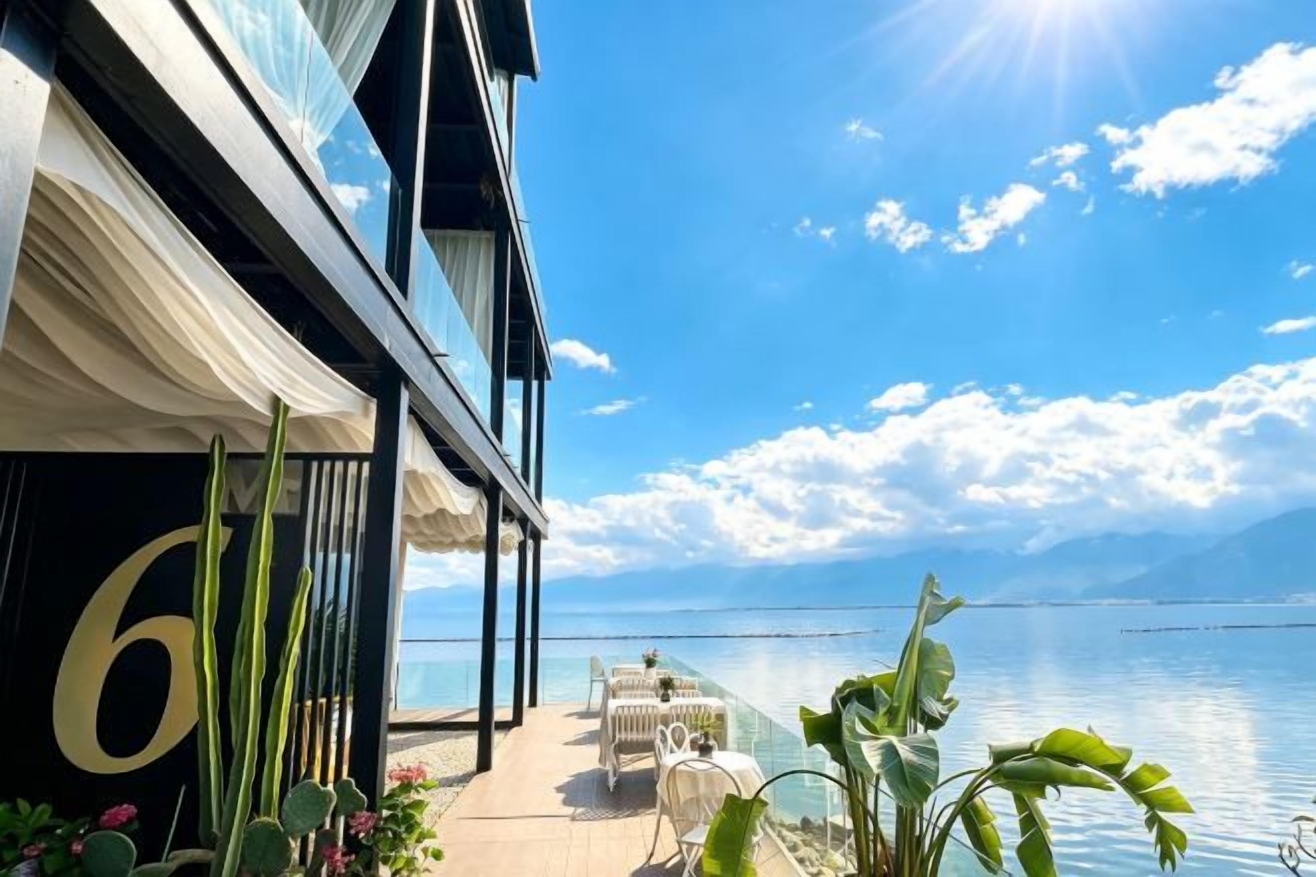 A balcony with a view of the sea, a table with chairs, and a building facade with a large number.