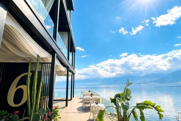 Un balcón con vista al mar, una mesa con sillas y fachada de edificio con un número grande.