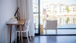 Una habitación con una mesa de madera, sillas blancas, vistas a edificios al otro lado del agua y un ventanal grande.