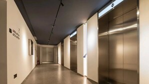 Un pasillo moderno con un ascensor metálico y un extintor en la pared.
