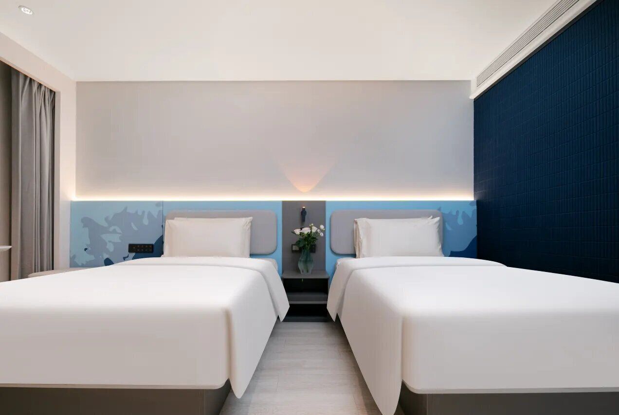 Habitación de hotel con dos camas, una mesita de noche, un florero y una lámpara fijada en la pared.