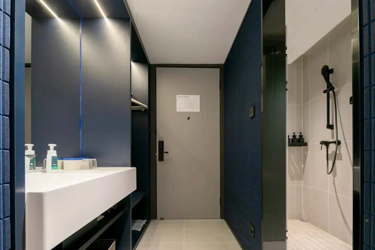 A modern bathroom with a white sink, a mirror, a shower area, and a door with a sign.