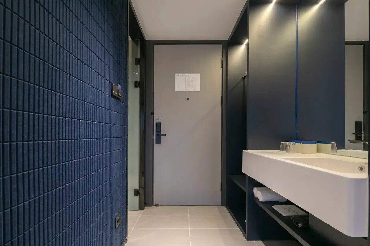 A modern bathroom with a dark blue tiled wall, a white sink, and a mirror.