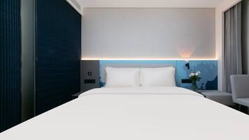 A hotel room with a large bed, a nightstand, a chair, and a wall-mounted lamp.