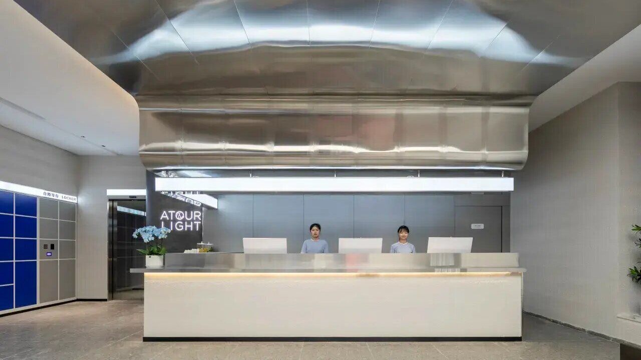Una reception dal design moderno, con due membri dello staff seduti dietro e un cartello con la scritta 'ATOUR LIGHT'.