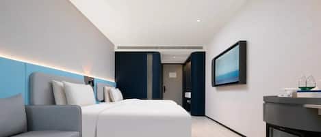 Quarto de hotel moderno com uma cama, área de estar, televisão e minibar.