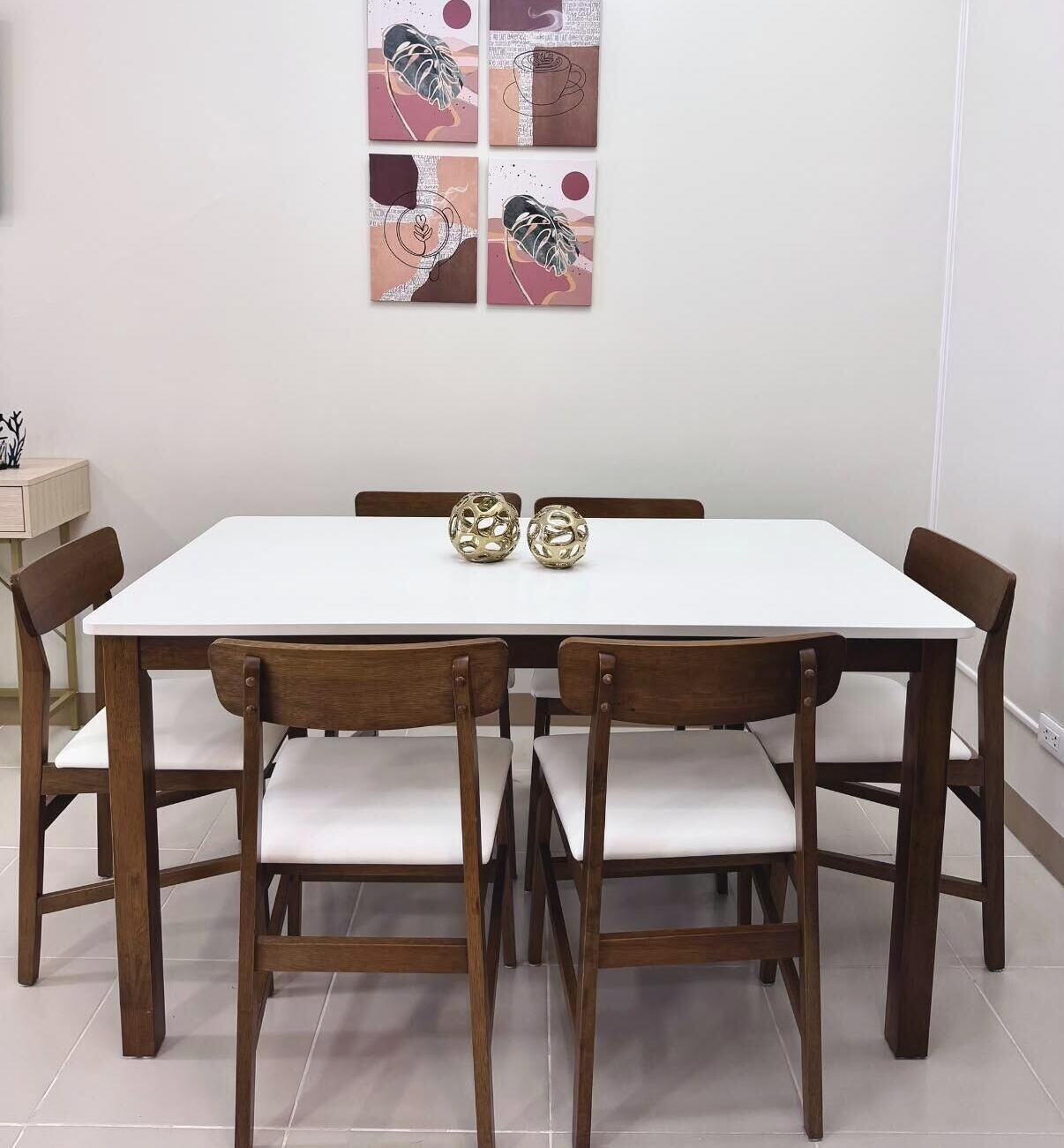 A dining table with four chairs, two decorative golden spheres, and a wall with abstract art.