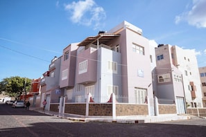 A multi-story residential building with a stone facade, multiple balconies, and a gated entrance. - Maya Apartment Studio (Mindelo)