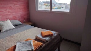 A bedroom with a bed, pillows, a window, and a view of buildings. - Maya Apartment Studio (Mindelo)