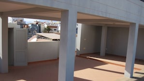 An empty covered outdoor area with tiled flooring and concrete pillars. - Maya Apartment Studio (Mindelo)