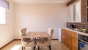 A compact kitchen with a dining table and chairs, a refrigerator, a stove, and a dishwasher. - Maya Apartment Studio (Mindelo)