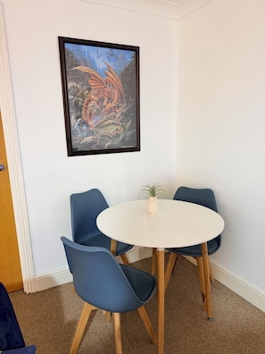 Ein Zimmer mit einem runden weißen Tisch, vier blauen Stühlen und einem gerahmten Kunstwerk an der Wand.