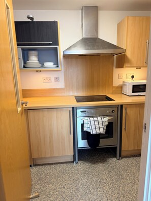 A compact kitchen with wooden cabinets, a stainless steel range hood, a microwave, and a built-in oven. - Stylish City-Centre Apartment Your Perfect Birmingham Base (Birmingham)