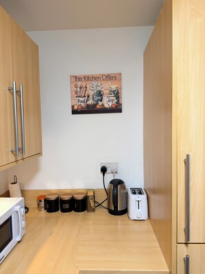 A compact kitchen with wooden cabinets, a kettle, a toaster, and a wall-mounted sign. - Stylish City-Centre Apartment Your Perfect Birmingham Base (Birmingham)