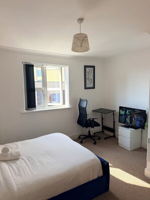 Ein Schlafzimmer mit einem Bett, einem Schreibtisch, einem Stuhl, einem Fernseher und einem Fenster mit Vorhängen.