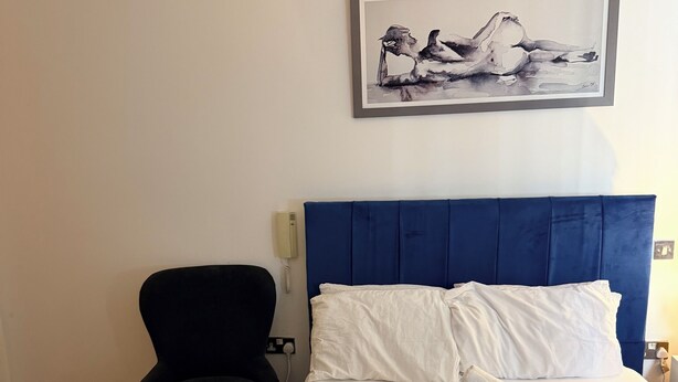 Ett hotellrum med en säng, en stol, en tavla på väggen och en telefon.
